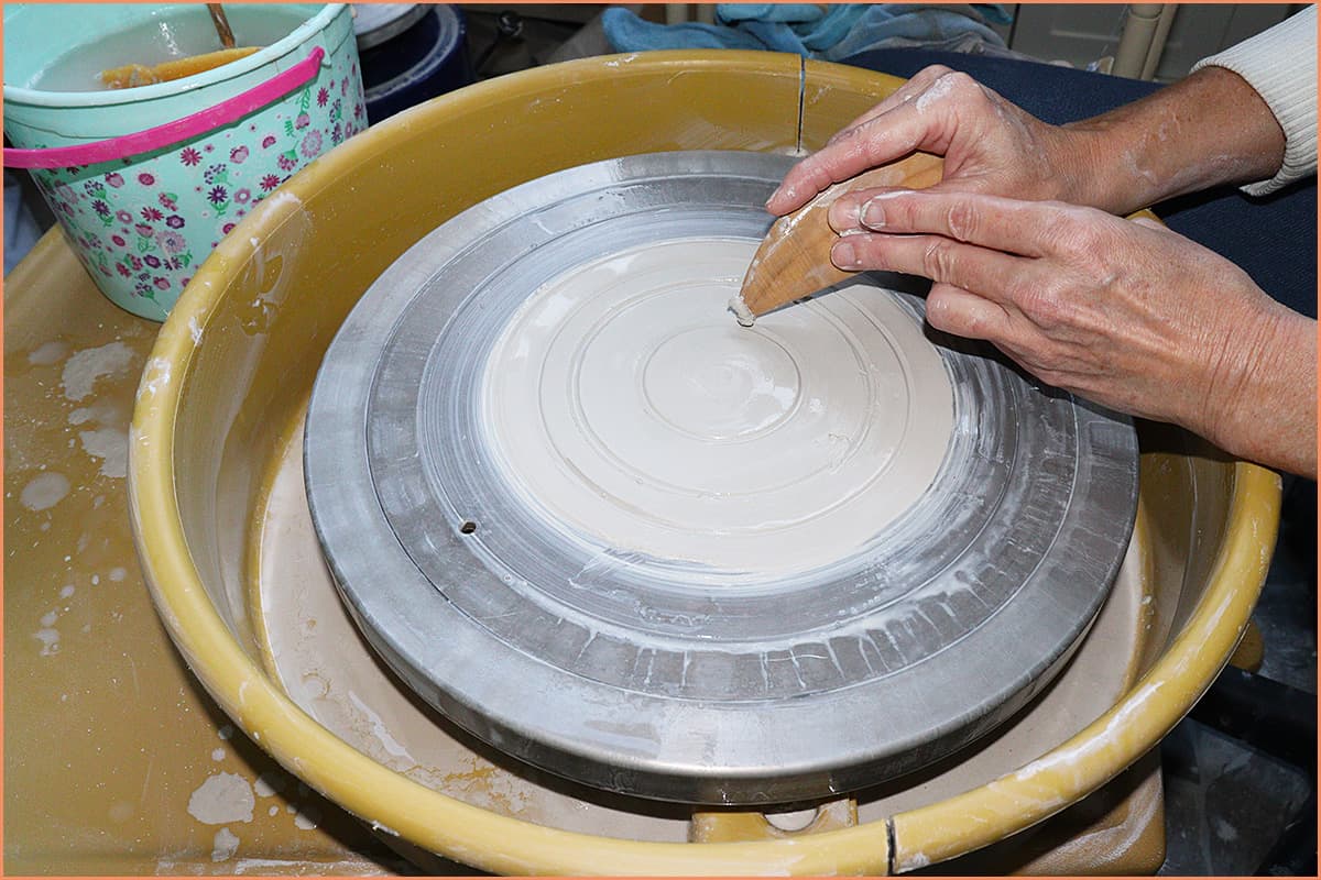 an image of a potter making several lines with clay on the wheel