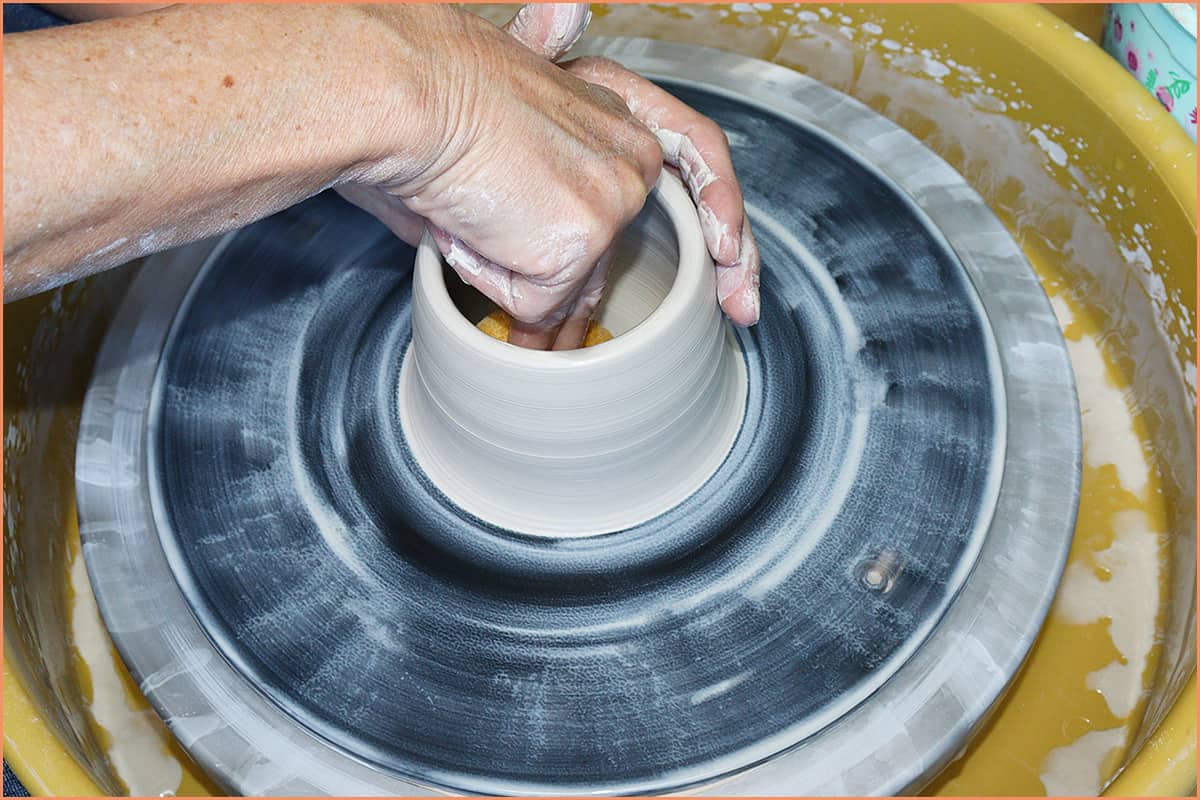 an image of a potter soaking up water on bottom of clay with sponge