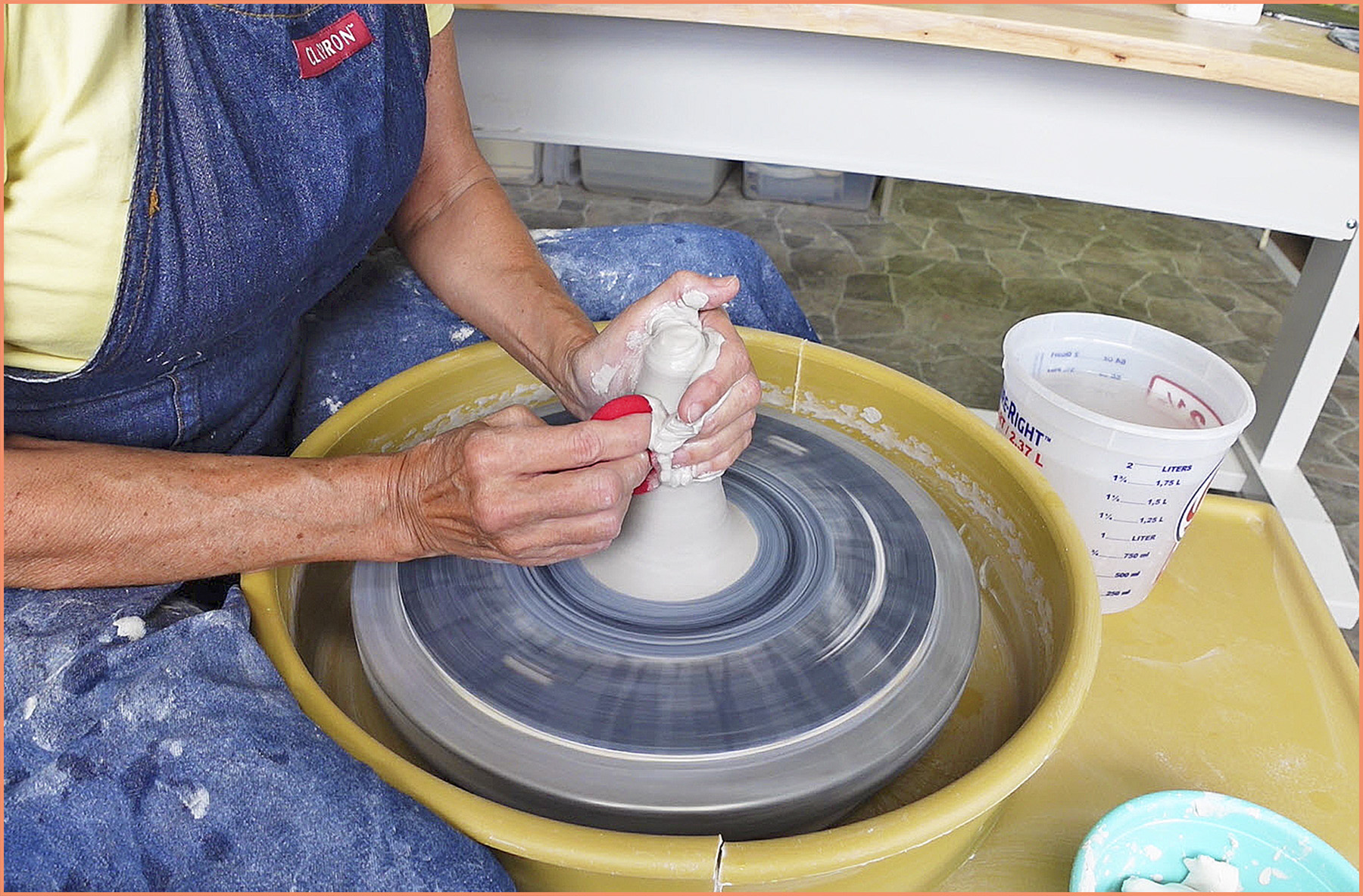an image of a potter using a sponge to cone up the clay on the pottery wheel